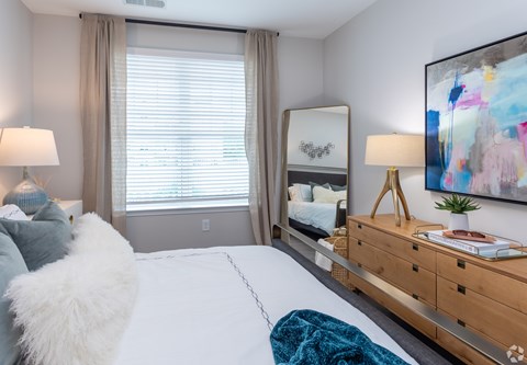 A bedroom with a large bed, a nightstand with a lamp, and a painting on the wall.
