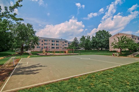 A basketball court is surrounded by grass and trees in front of a building.