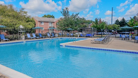 A large swimming pool with a blue tiled edge and a sun lounger area with blue sunshades.