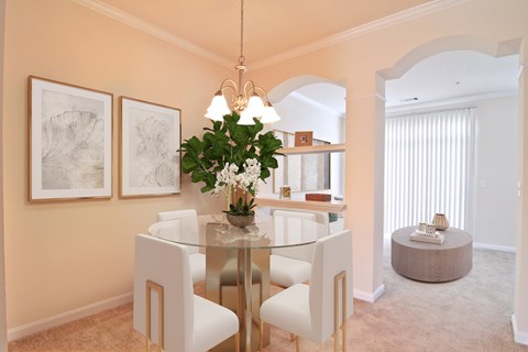 A dining room with a glass table and white chairs.