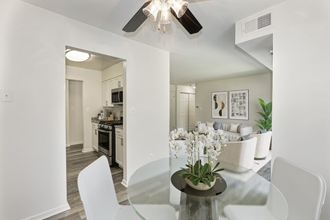 A modern dining room with a glass table and white chairs.