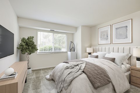 A bedroom with a large bed, a desk with a keyboard, and a plant.