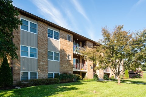 A brick apartment building with a balcony and a tree in front.