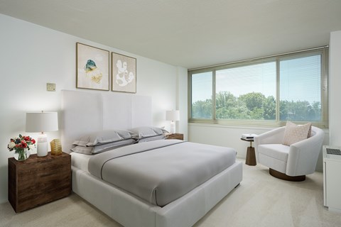 A bedroom with a large bed, a chair, and a window overlooking trees.