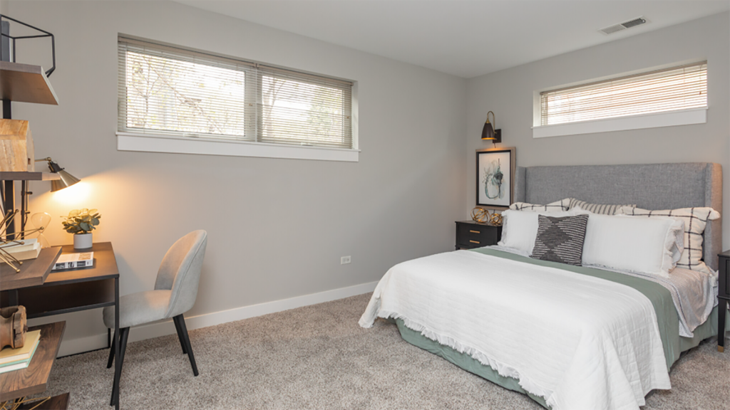 a bedroom with a bed and a desk and two windows