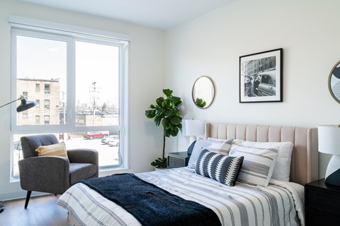 A bedroom with a bed, chair, and window.