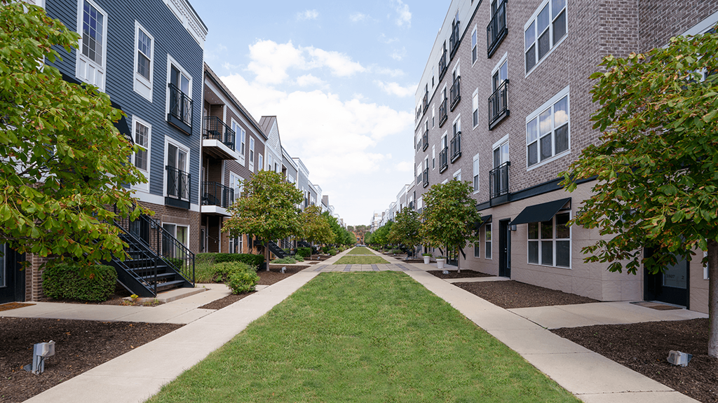 a grassy path between two apartment buildings with trees