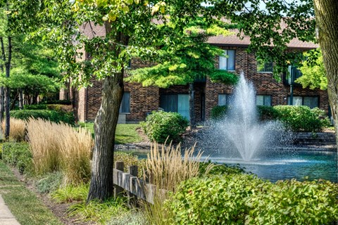 A fountain in the middle of a garden in front of a building.