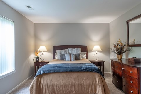A bedroom with a bed, two lamps, and a dresser.
