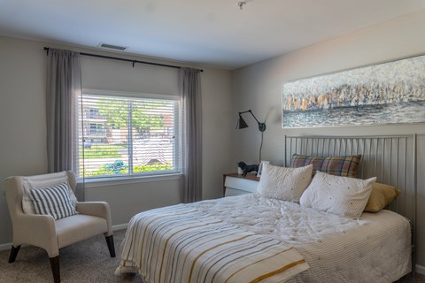 A bedroom with a large bed and a chair by the window.