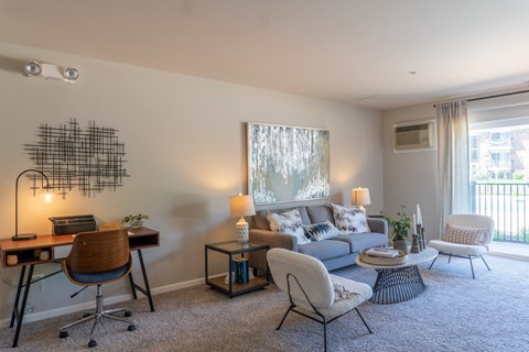 A well-lit living room with a grey sofa, a wooden desk, and a chair.