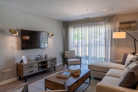 A well-lit living room with a wooden coffee table and a large window with curtains.