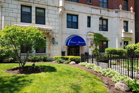 A white building with a blue awning and a black fence.