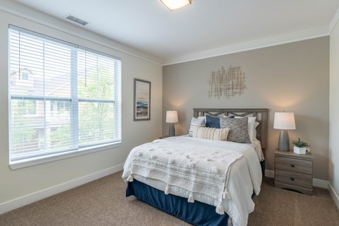 A bedroom with a large bed and a window with blinds.