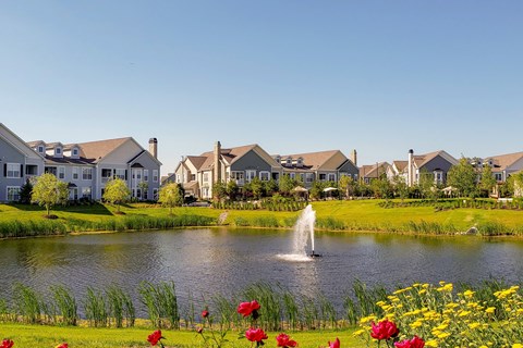 A serene lakeside scene with a fountain and houses in the background.
