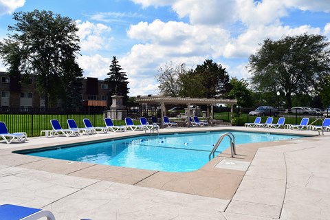 A swimming pool surrounded by chairs and trees.