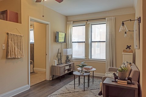 A living room with a brown couch, a coffee table, and a window with white curtains.