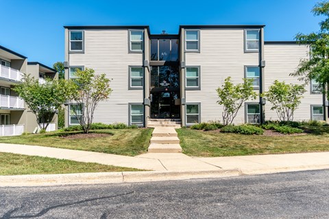 A modern apartment building with a glass entrance and a landscaped front yard.