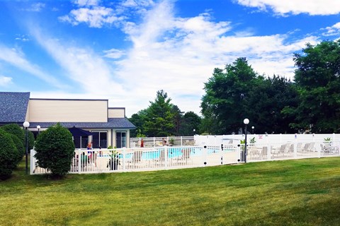 A pool surrounded by a white fence and a building in the background.
