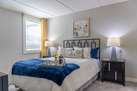 A bedroom with a bed, nightstand, and a painting on the wall.