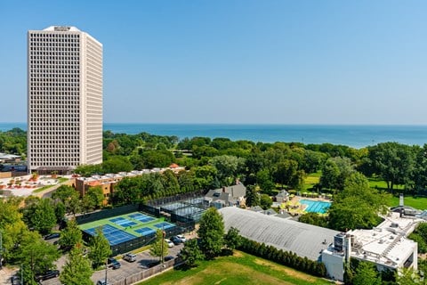 A tall building stands next to a tennis court and a pool.