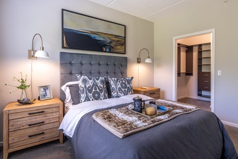 A bedroom with a large bed, a nightstand with a plant, and a painting on the wall.