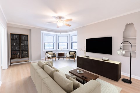 A living room with a large couch, a flat screen TV, and a ceiling fan.