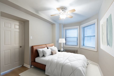 A bedroom with a bed, pillows, a ceiling fan, and a window with blinds.