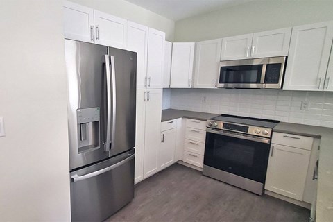 A kitchen with a stainless steel refrigerator and oven, white cabinets, and a black and white tiled backsplash.