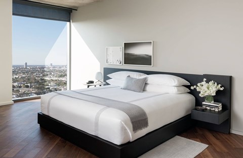 A bedroom with a large bed and a city view through the window.