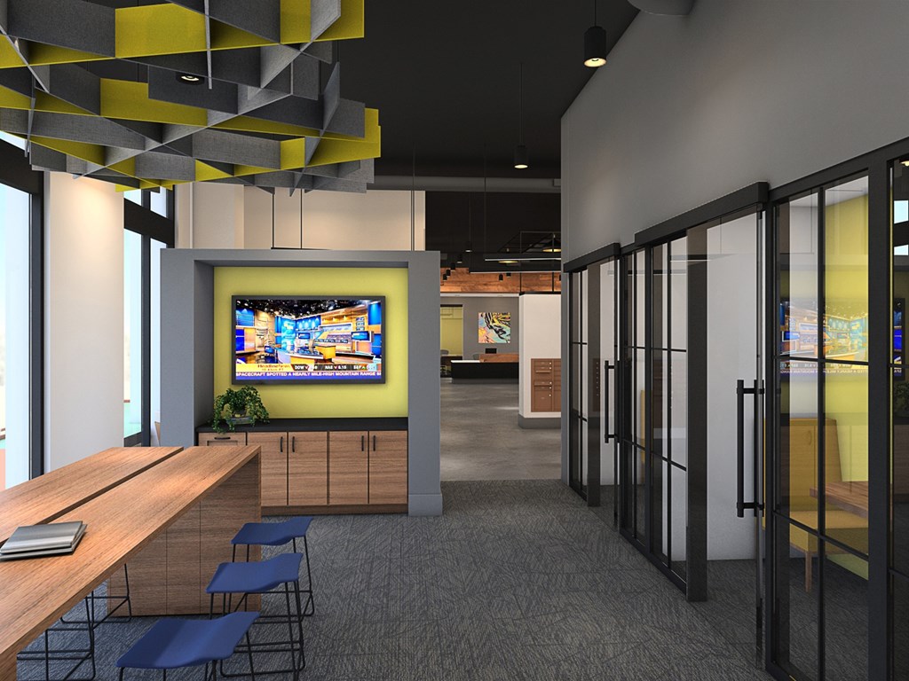 A modern office space with a TV mounted on the wall and a long wooden table with chairs.