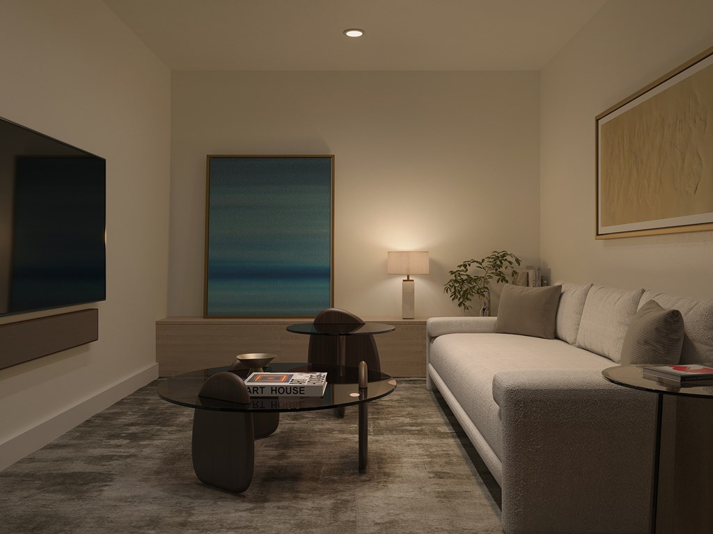 A living room with a grey couch, a glass coffee table, and a painting on the wall.