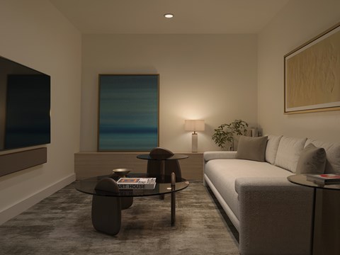A living room with a grey couch, a glass coffee table, and a painting on the wall.