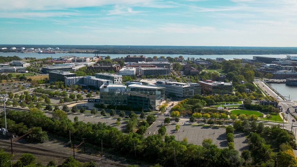A large building complex sits in the middle of a green area with a body of water in the background.