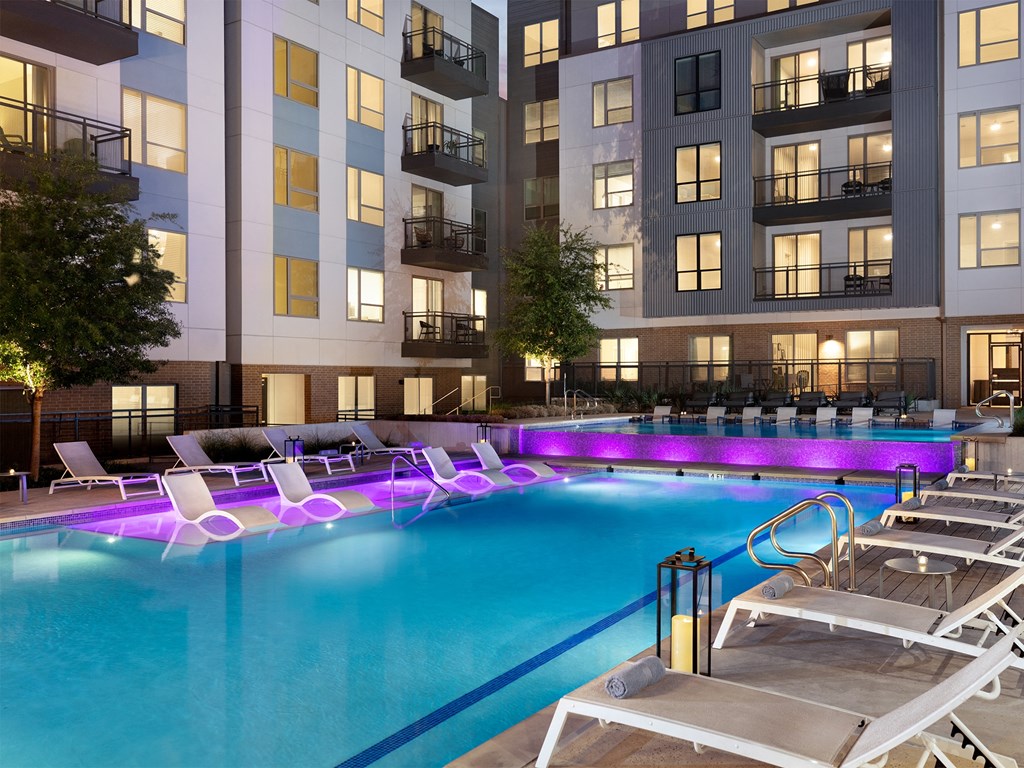a pool with lounge chairs in front of an apartment building
