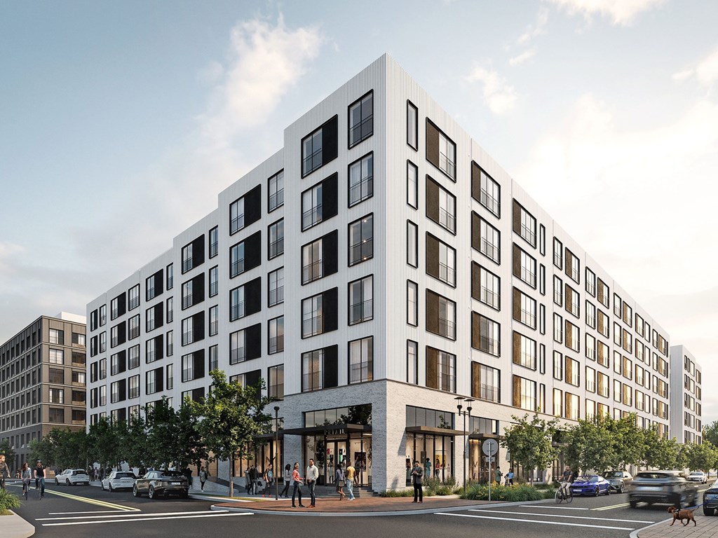 A modern white building with black windows is situated on a street corner with cars and people around it.