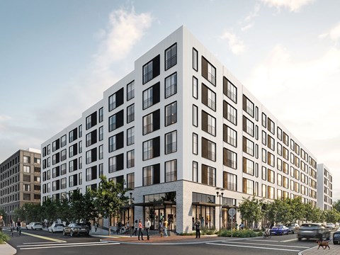 A modern white building with black windows is situated on a street corner with cars and people around it.