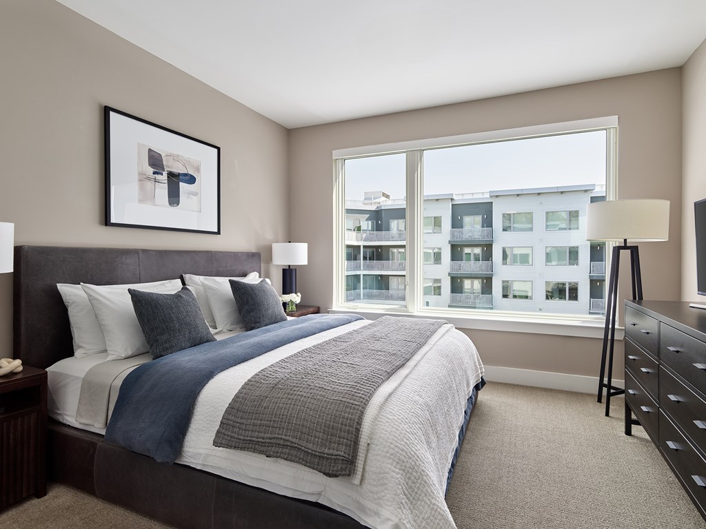 A bedroom with a large bed and a view of a building outside the window.