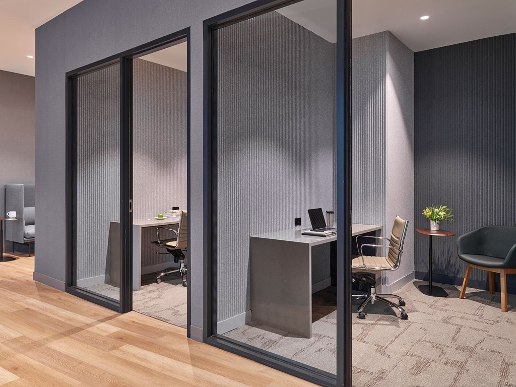 A modern office with a glass partition wall and a wooden floor.