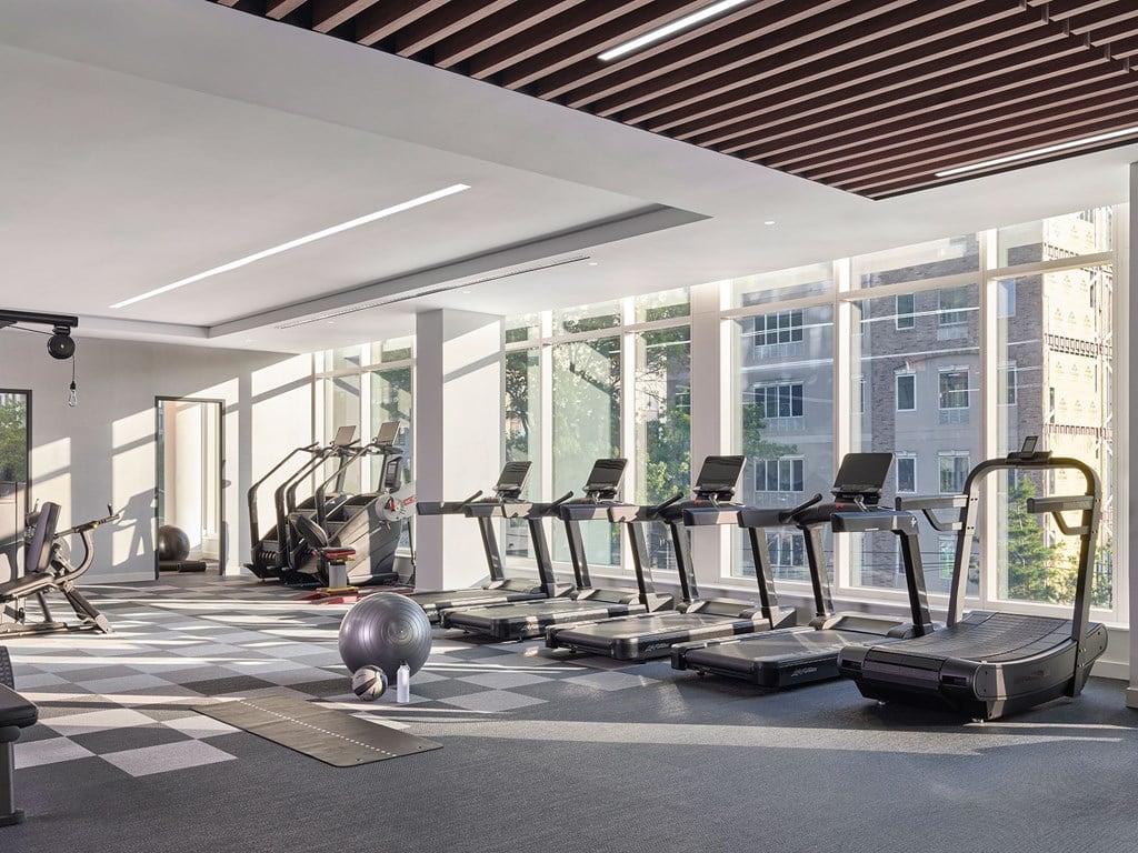 A gym with treadmills, exercise bikes, and a large window overlooking a cityscape.