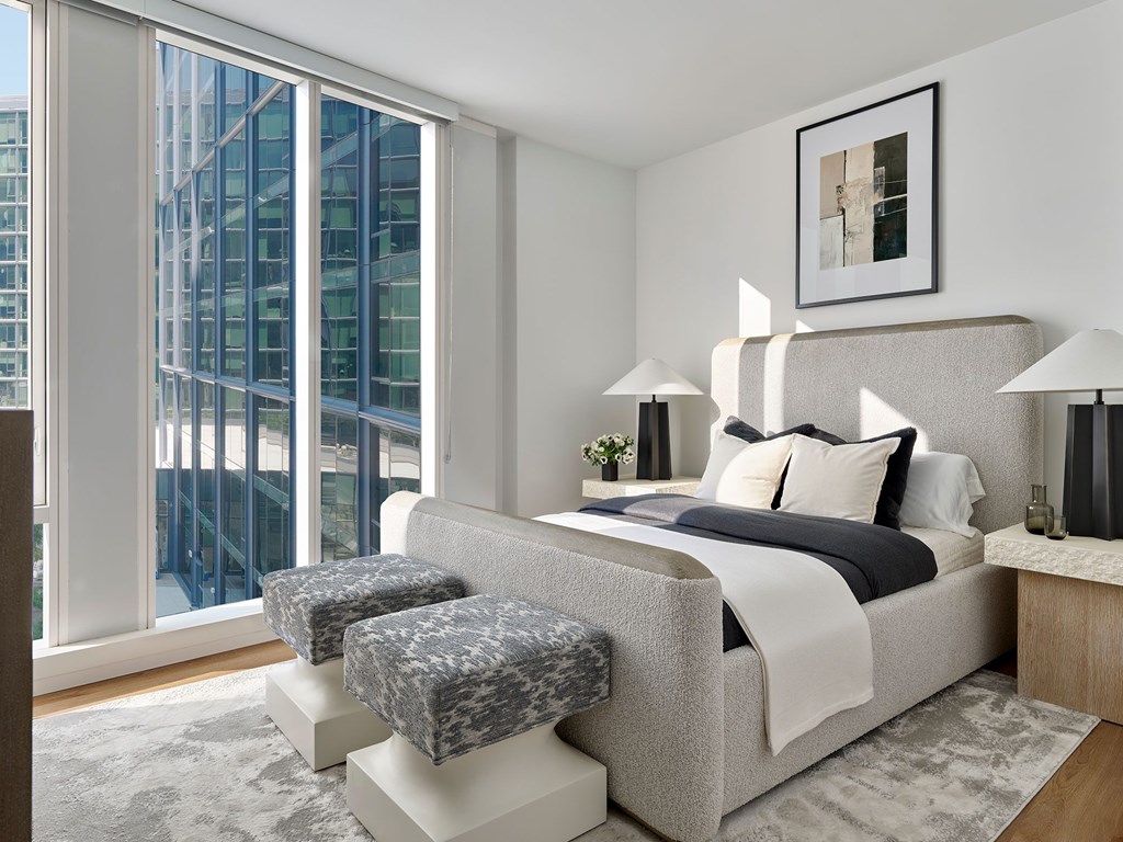 A modern bedroom with a large bed and a view of a cityscape through the window.