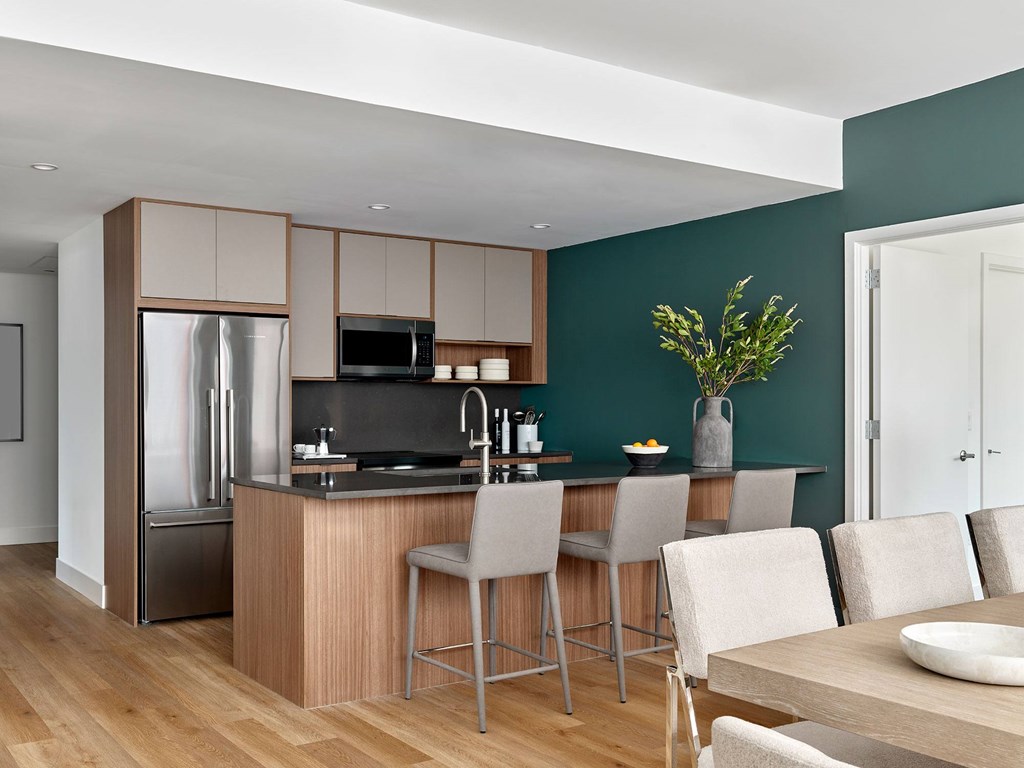 A modern kitchen with a refrigerator, sink, and bar stools.