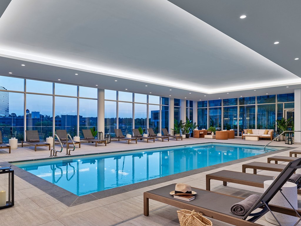 A large indoor swimming pool with lounge chairs and a table with a hat and a book.