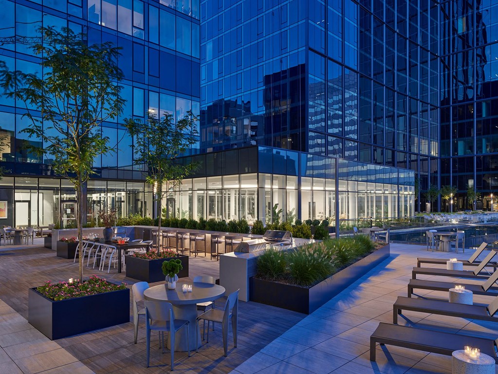 A rooftop patio with tables and chairs is illuminated by lights.