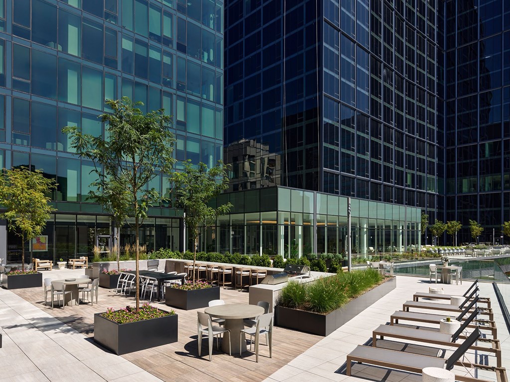 A modern outdoor seating area with tables and chairs is surrounded by tall buildings.
