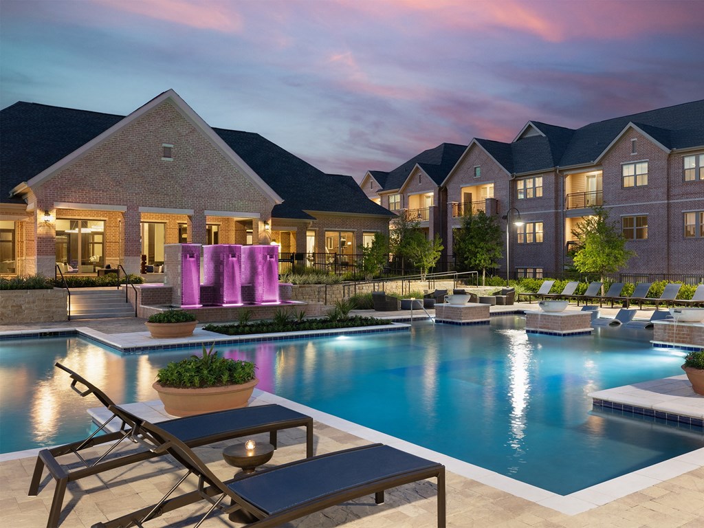 a swimming pool with lounge chairs and a fountain in front of an apartment building