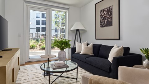 A living room with a black couch, a glass table, and a television.