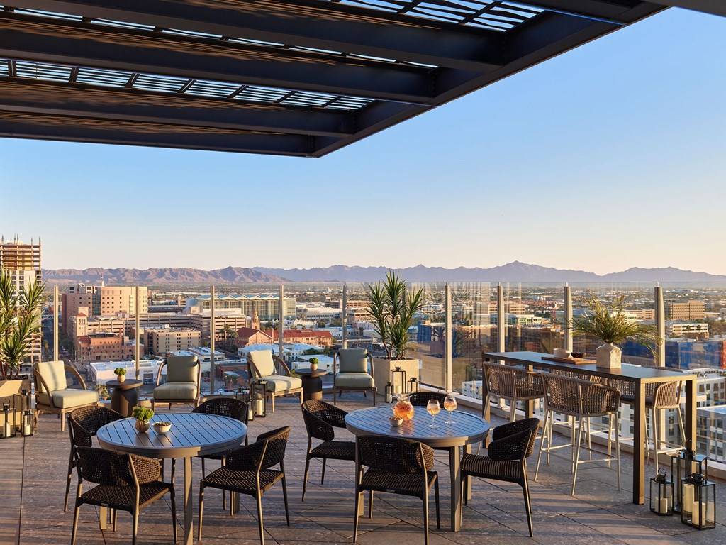 A rooftop patio with tables and chairs overlooking a cityscape.