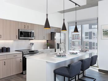 A modern kitchen with a white countertop and black chairs.