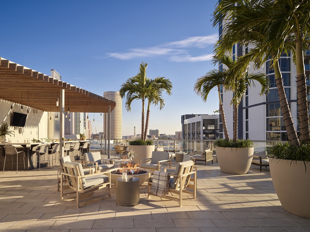 A patio with chairs and tables is surrounded by palm trees.